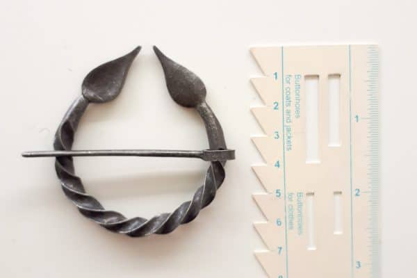 A twisted metal fibula with leaves next to a ruler